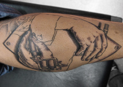 Realistic tattoo of two hands drawing and tattooing each other into existence, after the work of artist M.C. Escher.